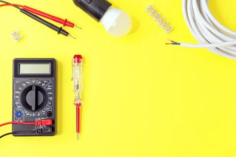 Digital multimeter and indicator screwdriver on a yellow background. Stock Photos