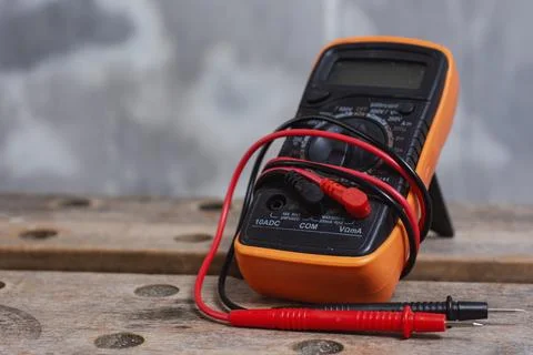 Digital multimeter with red and black test leads placed on wooden workbench.  Stock Photos