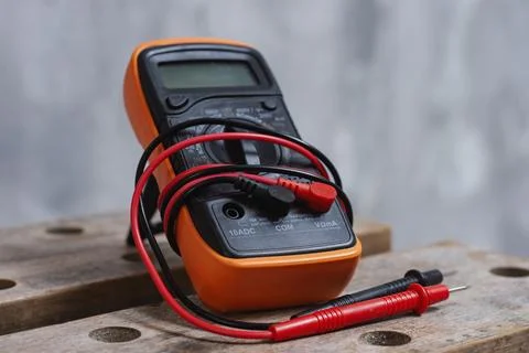 Digital multimeter with red and black test leads placed on wooden workbench.  Stock Photos