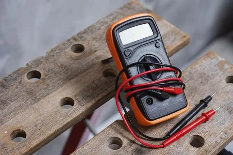Digital multimeter with red and black test leads placed on wooden workbench.  Stock Photos