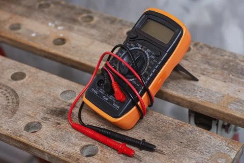 Digital multimeter with red and black test leads placed on wooden workbench.  Stock Photos