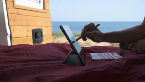 Digital nomad drawing on a tablet inside a campervan with sea view Stock Footage 334280730