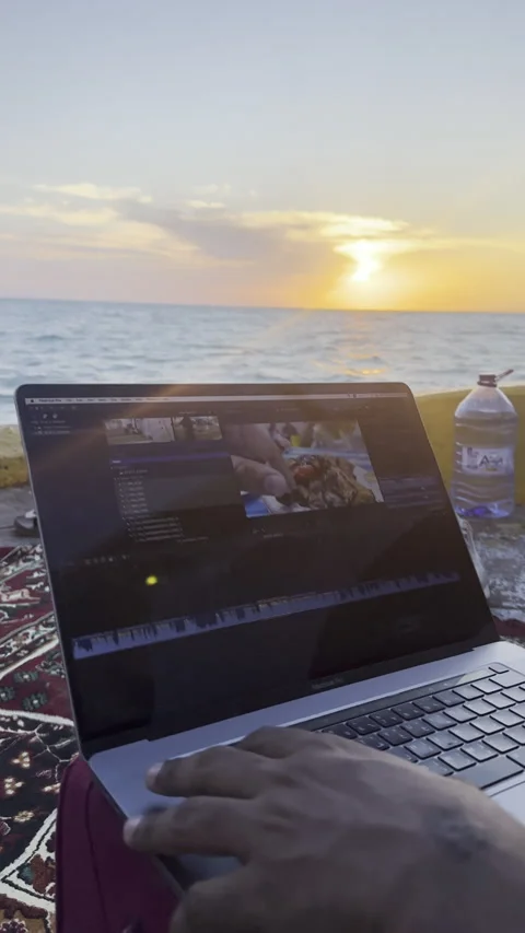 A Digital Nomad Editing on a Laptop by the Ocean at Sunset Stock Footage 323614331