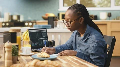 Digital nomad writing research data from charts, laptop displaying analytics Stock Photos