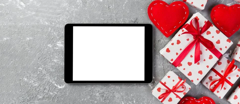 Digital tablet blank screen with gift box and hearts decor on gray cement tab Stock Photos