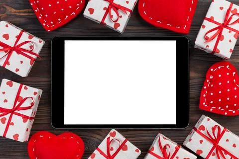 Digital tablet blank screen with gift box and hearts decor on wooden table... Stock Photos