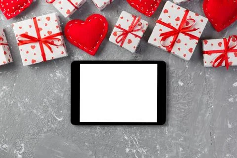 Digital tablet blank screen with gift box and hearts decor on gray cement t.. Stock Photos