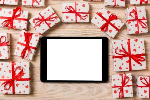 Digital tablet blank screen with gift box and hearts decor on wooden table... Stock Photos