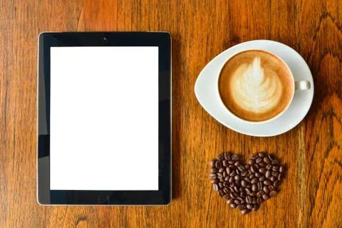Digital tablet pc and a cup of coffee with heart shape on wood background Stock Photos