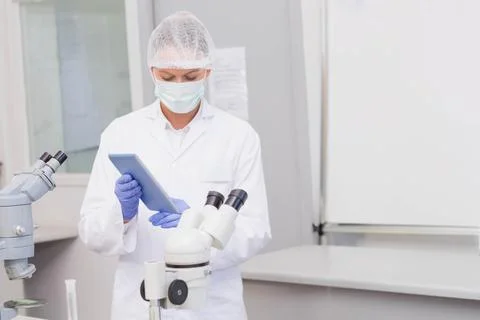 Digital tablet showing data on clean lab bench beside two compound microscopes Foto stock