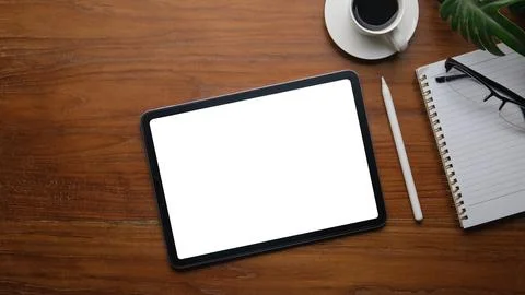 Digital tablet with white screen, coffee cup, glasses and notepad on wooden.. Stock Photos