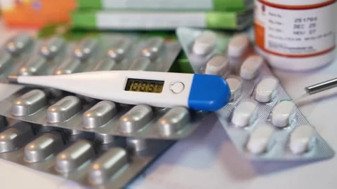 Digital thermometer lying on blister packs of pills and medicine bottle, cl.. Video stock 330547503