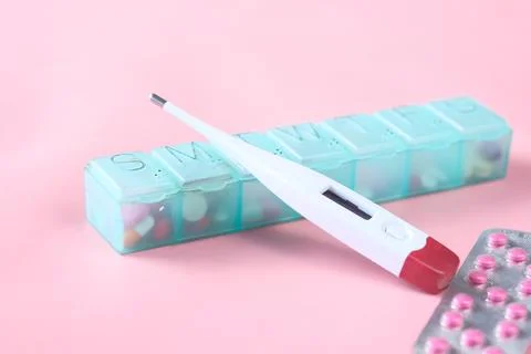 Digital thermometer, pill container on a pink background Stock Photos