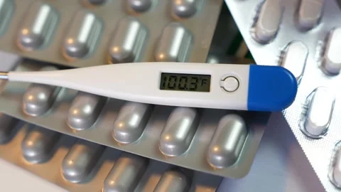 Digital thermometer showing 100.3f lying on blister packs of capsules and p.. Stock Footage 330547505