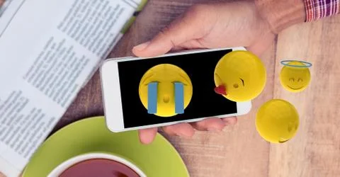 Digitally generated image of emojis flying over hand holding smart phone at Stock Photos