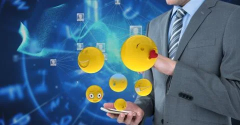 Digitally generated image of emojis flying by businessman using smart phone Foto stock