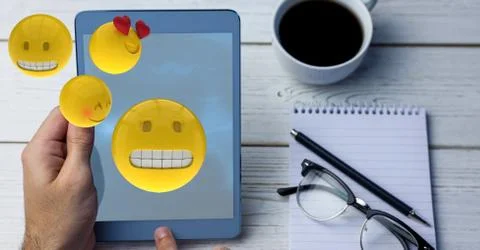 Digitally generated image of emojis flying over hand using digital tablet by Stock Photos