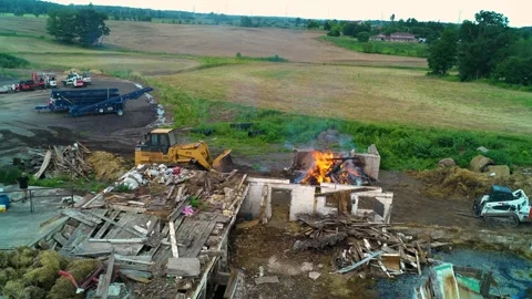 A dilapidated barn with a track loader adding wood and debris to a fire Stock Footage 327392614