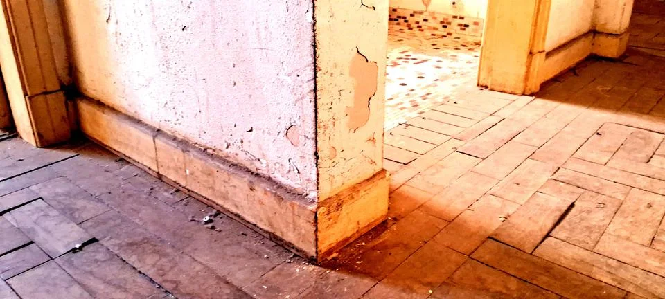 Dilapidated interior corner featuring weathered wooden floors and peeling paint Stock Photos