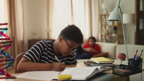 Diligent African American boy studying while lazy sister plays video games Stock Footage 334947908