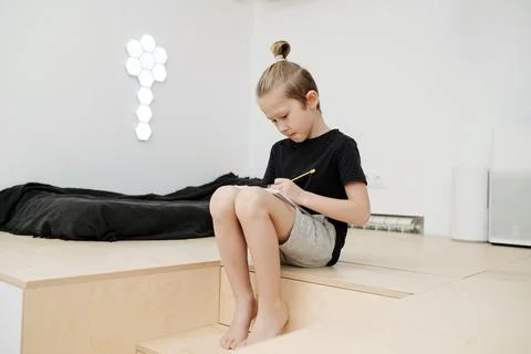 Diligent boy is sitting on a step of a stair, writing something on his knees. Stock Photos