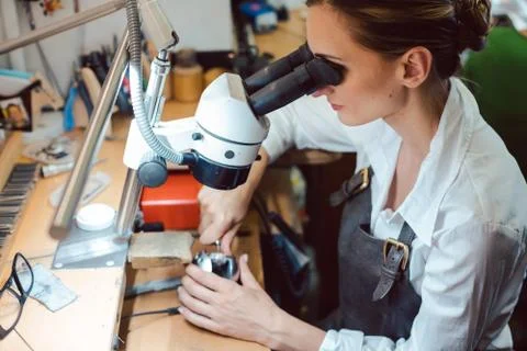 Diligent jeweler working on microscope at her workbench Stock Photos