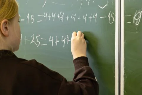 A diligent schoolchild writes complex math equations on a green chalkboard .. Stock Photos