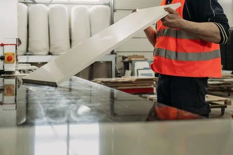 A diligent worker in high-visibility gear carefully handles a long sheet of m Stock Photos