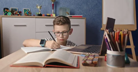 Diligent Young Boy Focused on Writing Homework with Laptop and Books Stock-Footage 267629579