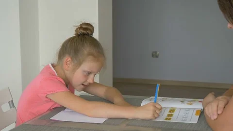 Diligent young schoolgirl is doing homework with help from her mother Stock Footage