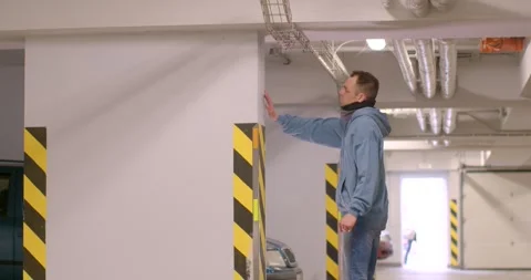 In a dim garage, a man measures a wall and assesses the ceiling Stock Footage 311816769
