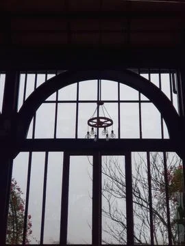 Dim interior view through large arched window with chandelier, foggy exterior Stock Photos
