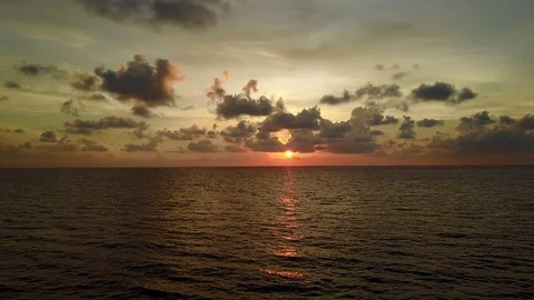 Dim sunset over tropical sea, red sun shine low over horizon line, dark clouds Stock Footage 80378657