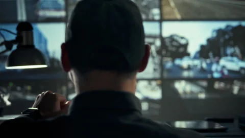 In dim video-surveillance hub an operator scans rows of monitoring screens m Stock Footage 336570462