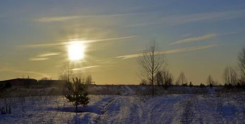 The dim winter sun sets over the horizon on an endless snow-covered field Stock Photos