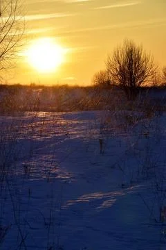The dim winter sun sets over the horizon on an endless snow-covered field Stock Photos