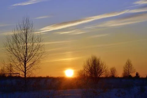 The dim winter sun sets over the horizon on an endless snow-covered field Stock Photos