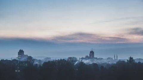 Dim winter twilight. Clouds at sunset over dark industrial town. Stock Photos
