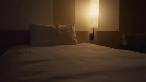 Dimly lit and empty hotel bedroom with a bedside lamp casting a warm glow Vidéo 344395475