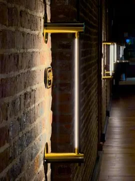 Dimly lit brick wall with brass wall-mounted fixtures and glowing vertical light Stock Photos