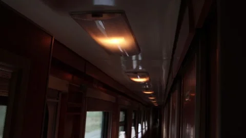 Dimly lit corridor of a moving passenger train. Warm overhead lights illuminate Stock Footage 318289464