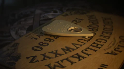 Dimly lit Ouija board planchette resting on letters Stock Footage 333646110