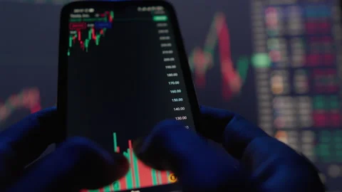 In a dimly lit room, using a smartphone for stock analysis and trading, tracking Stock Footage 285842953