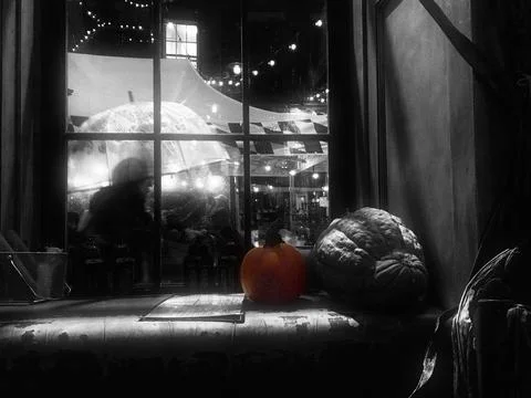 A dimly lit scene through a window shows pumpkins on a ledge with a figure .. Stock Photos