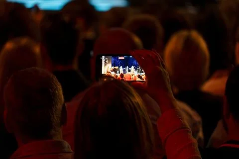 In a dimly lit setting with red lighting, someone captures a stage show on a Stock Photos