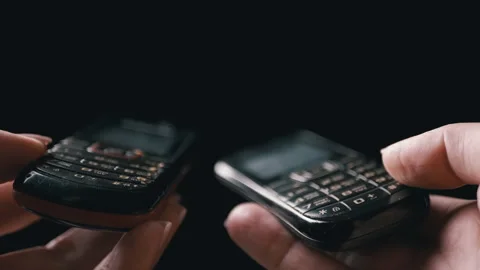 In a Dimly Lit Space, Two Old Push-Button Mobile Phones Exchange Information Stock Footage 312014463
