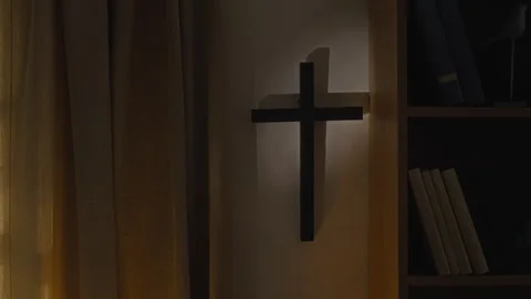 Dimly Lit Wall with Black Cross Casting Shadow next to Curtain and Bookcase Stock Footage 327382880