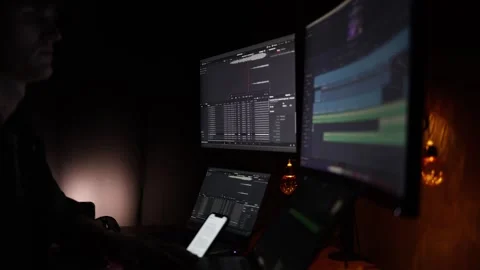 A dimly lit workspace featuring multiple monitors displaying video editing timel Stock Footage 297112144