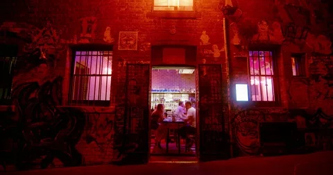 Diners in a red-lit graffiti laneway restaurant at night, Melbourne Stock Footage 85250120
