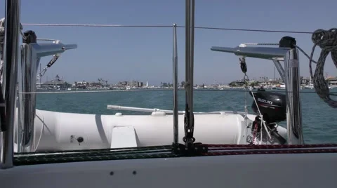Dinghy on davits behind catamaran with ropes tied to life lines sailing in ha Stock Footage 67491038
